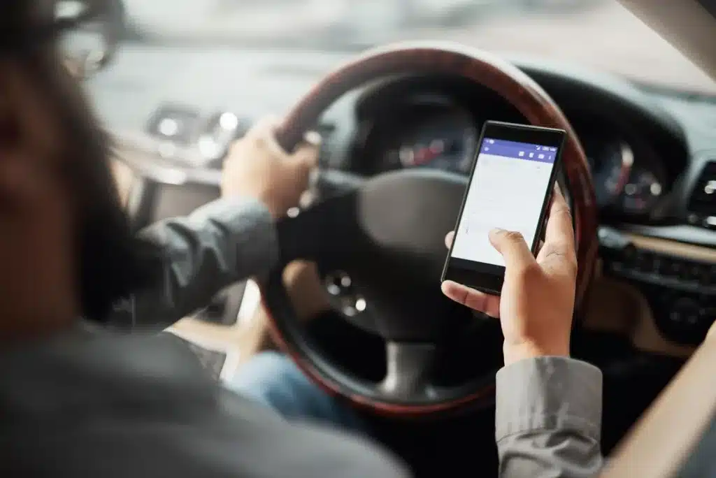 Driver using a smartphone while steering a car, illustrating a major cause of car accidents in Texas.