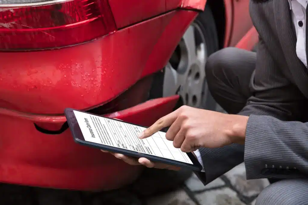 Person filing an insurance claim on a tablet beside a damaged car after a Florida accident