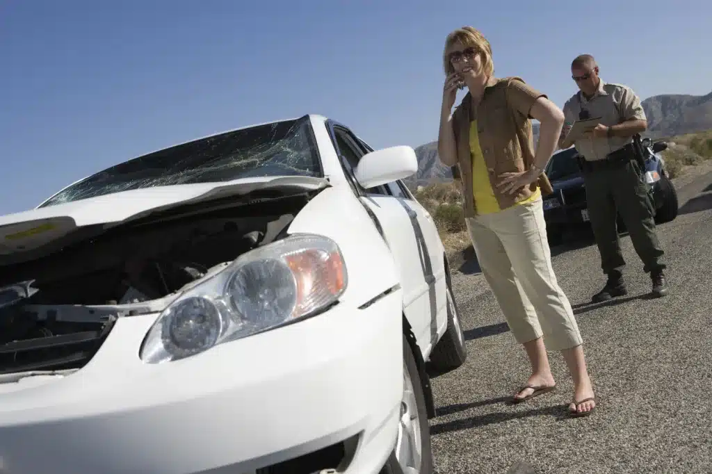 Woman on phone beside damaged car after accident with police officer