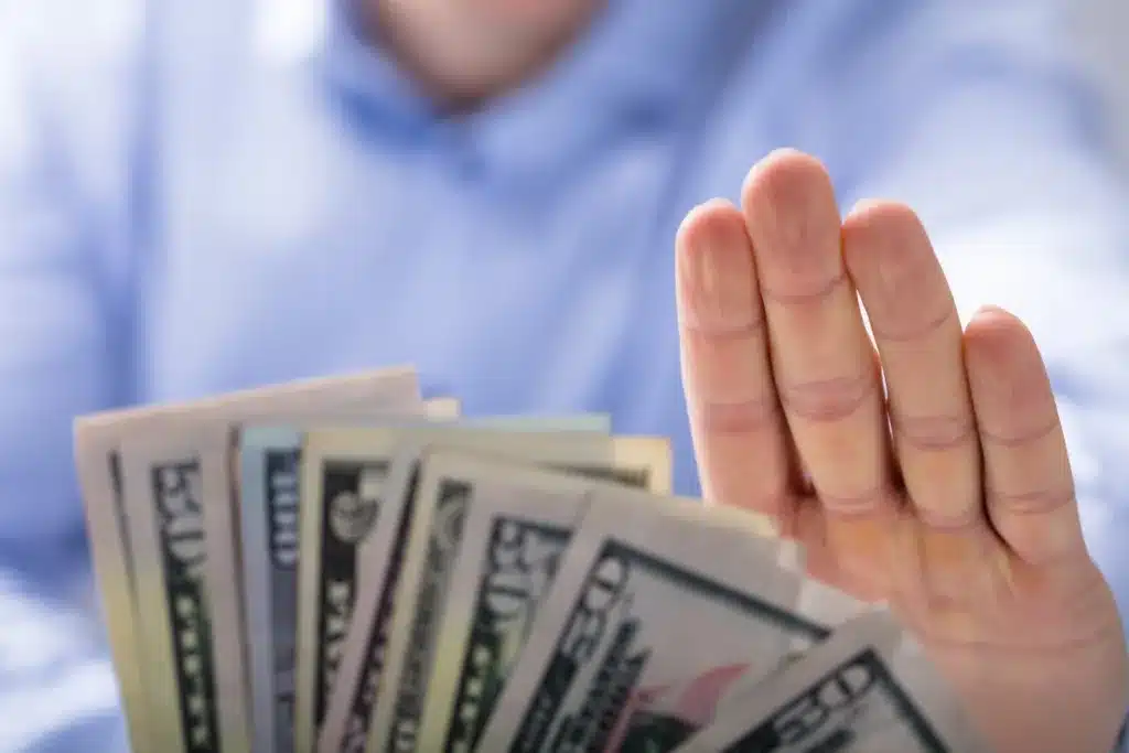 A hand making a stop gesture toward a fan of cash, illustrating whether an injured worker should accept a Florida workers' comp settlement.