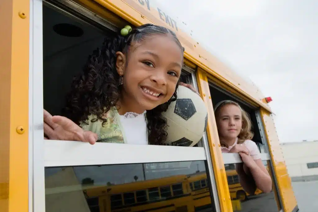 A smiling young girl looking out of a school bus window, highlighting the importance of preventing common causes of school bus accidents.