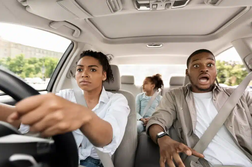 A concerned woman driving a car with three passengers looking stressed, illustrating how car insurance limits work when multiple people are injured in the same crash.